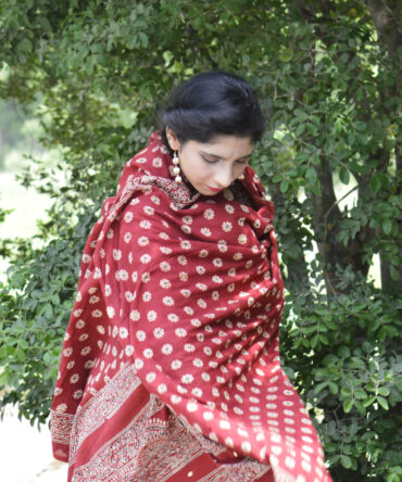 Close-up view of the hand block printing technique on the Ajrak Odhni, highlighting the detailed craftsmanship and rich organic dye patterns in red and earth tones.