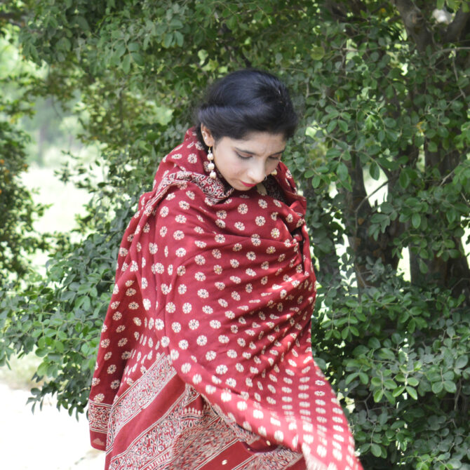 Close-up view of the hand block printing technique on the Ajrak Odhni, highlighting the detailed craftsmanship and rich organic dye patterns in red and earth tones.