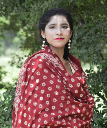 A vibrant Organic Dye Hand Block Printed Ajrak Odhni Margarita Floral showcasing intricate geometric and floral patterns in deep red hues, draped elegantly over a wooden chair.