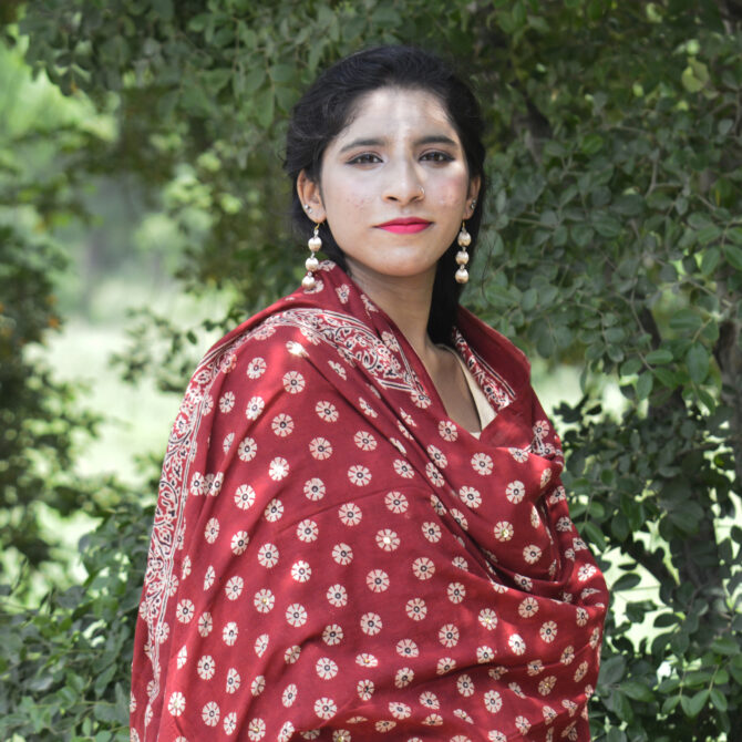 A vibrant Organic Dye Hand Block Printed Ajrak Odhni Margarita Floral showcasing intricate geometric and floral patterns in deep red hues, draped elegantly over a wooden chair.