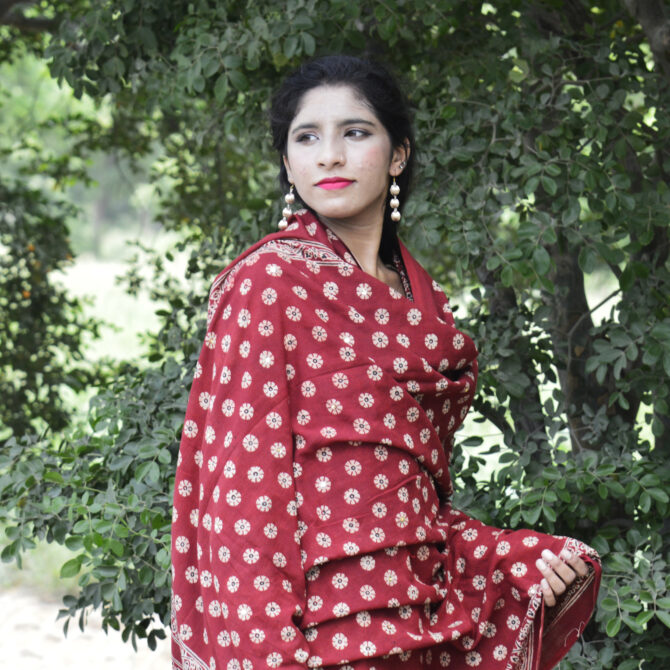 A woman wearing the Organic Dye Hand Block Printed Ajrak Odhni Margarita Floral as a stylish dupatta, complementing her traditional outfit with its luxurious fabric and intricate designs.