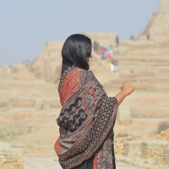 A beautifully draped Organic Dye Hand Block Printed Ajrak Odhni featuring intricate geometric and floral patterns in red and black on high-quality lawn cotton.