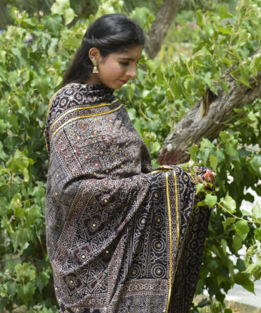 A beautiful Organic Dye Hand Block Printed Ajrak Chaadar Multi Blocks draped elegantly over a model, showcasing intricate floral and geometric designs in deep black.