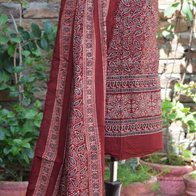 Close-up of a maroonish red un-stitched fabric, adorned with detailed Ajrak Kerry hand block prints, dyed using organic materials, representing a blend of cultural heritage and modern fashion.