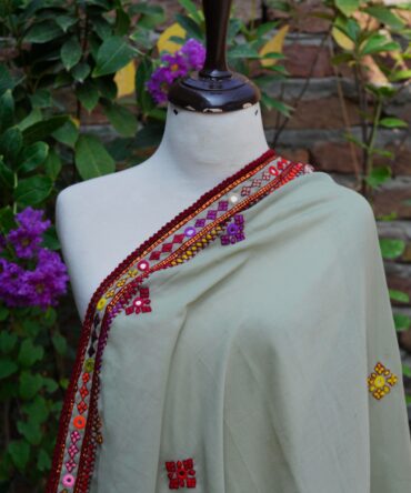 Close-up view of intricate mirror work and colorful embroidery on a pista green Sindhi chaadar, highlighting the fine craftsmanship of rural Sindhi artisans.