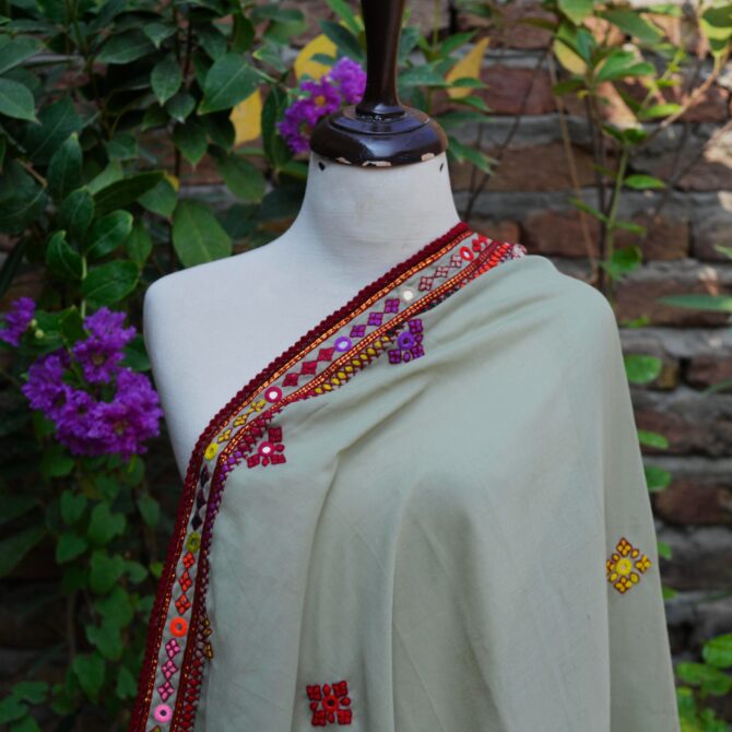 Close-up view of intricate mirror work and colorful embroidery on a pista green Sindhi chaadar, highlighting the fine craftsmanship of rural Sindhi artisans.