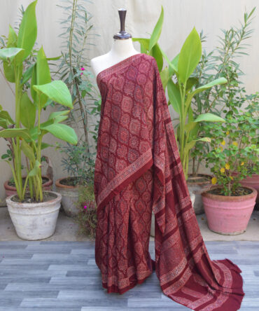 Ethnic Ajrak Saree in Reddish Maroon draped on a model, featuring intricate hand block patterns with geometric and floral designs, crafted from soft Modal Silk for elegance and comfort.