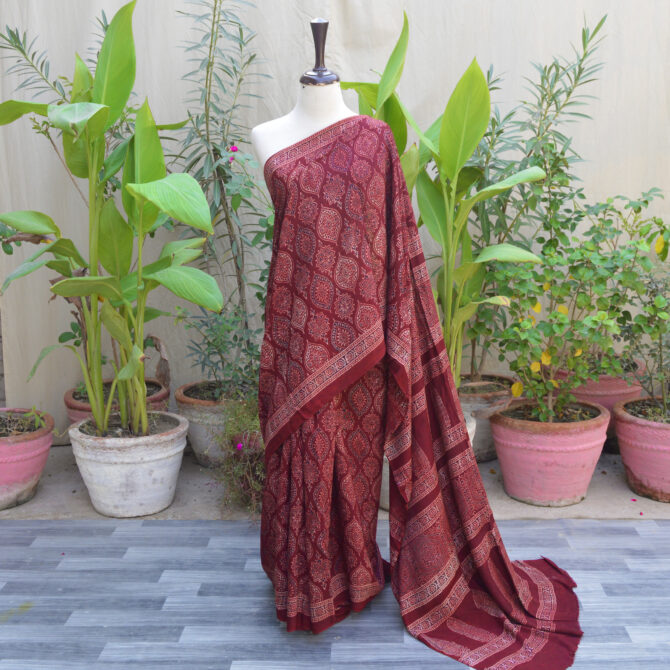 Ethnic Ajrak Saree in Reddish Maroon draped on a model, featuring intricate hand block patterns with geometric and floral designs, crafted from soft Modal Silk for elegance and comfort.