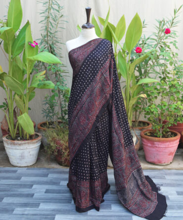 A beautifully handcrafted Ethnic Ajrak Saree with polka dot patterns in deep black, blending traditional Ajrak block printing with modern design. Made from breathable, eco-friendly Modal Silk with intricate geometric and floral motifs.