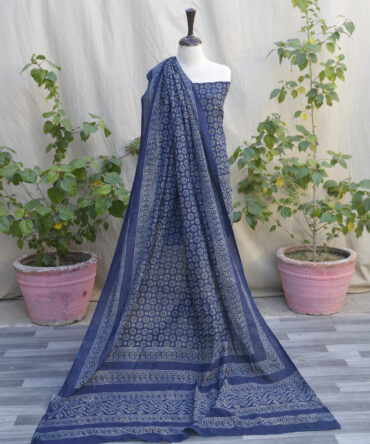 A vibrant Ajrak Floral Indigo fabric draped gracefully, showcasing intricate patterns in indigo and floral motifs. The piece highlights traditional craftsmanship with a modern appeal.